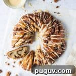 Vegan Maple Pecan Bread Wreath Recipe for Holiday Brunch 7 Maple pecan bread wreath with two slices cut out on a sheet of baking parchment with a bowl of glaze, pecan nuts and mini bottles of maple syrup.