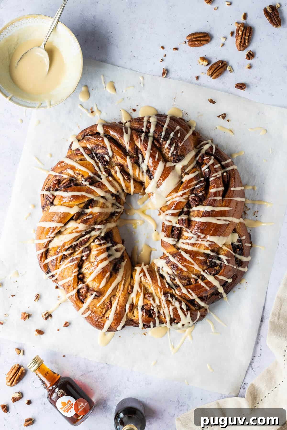 Maple pecan bread wreath – this impressive vegan maple pecan couronne is a real showstopper which would be perfect for an indulgent breakfast or brunch. #veganbaking #eggless #dairyfree #bread #veganbreakfast #veganbrunch Maple pecan bread wreath from above on a sheet of baking parchment on a grey background.