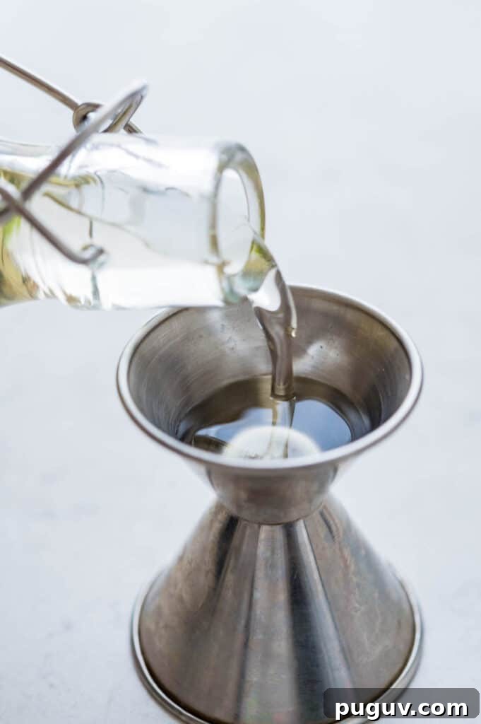 pouring sugar syrup recipe into a cocktail jigger.