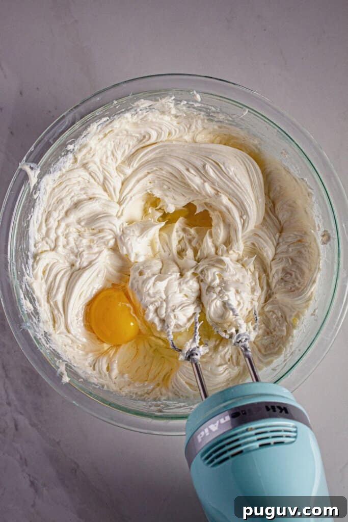 Decadent RumChata Cheesecake Recipe: Creamy Liqueur Dessert 6 Eggs being mixed into cream cheese.