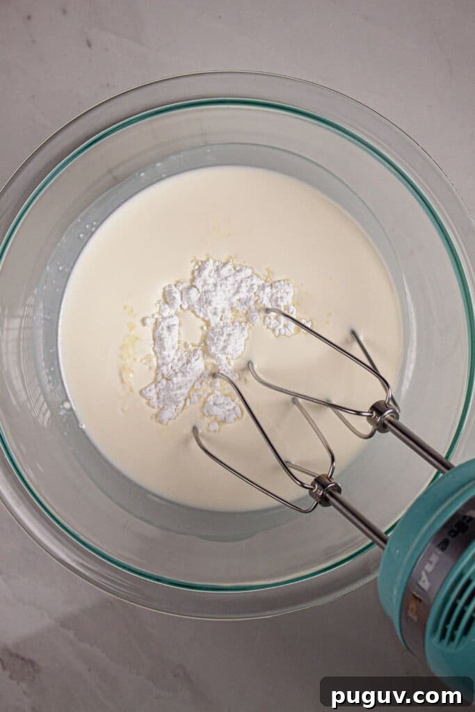 Decadent RumChata Cheesecake Recipe: Creamy Liqueur Dessert 9 Heavy cream and powdered sugar being whipped in a glass bowl.