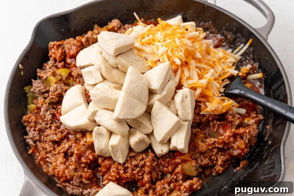 The biscuit pieces and shredded cheese are added to the pan.