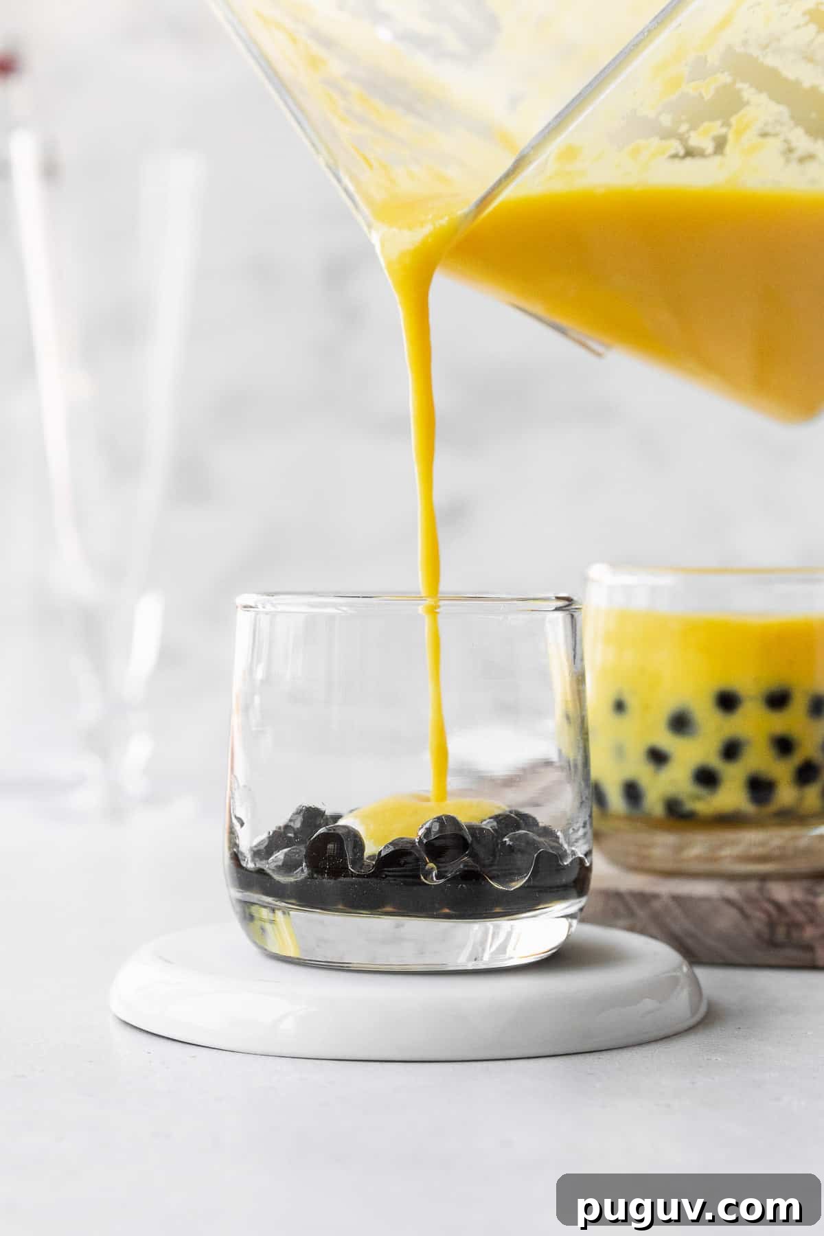 Pouring the mango puree into a small glass with the boba pearls.