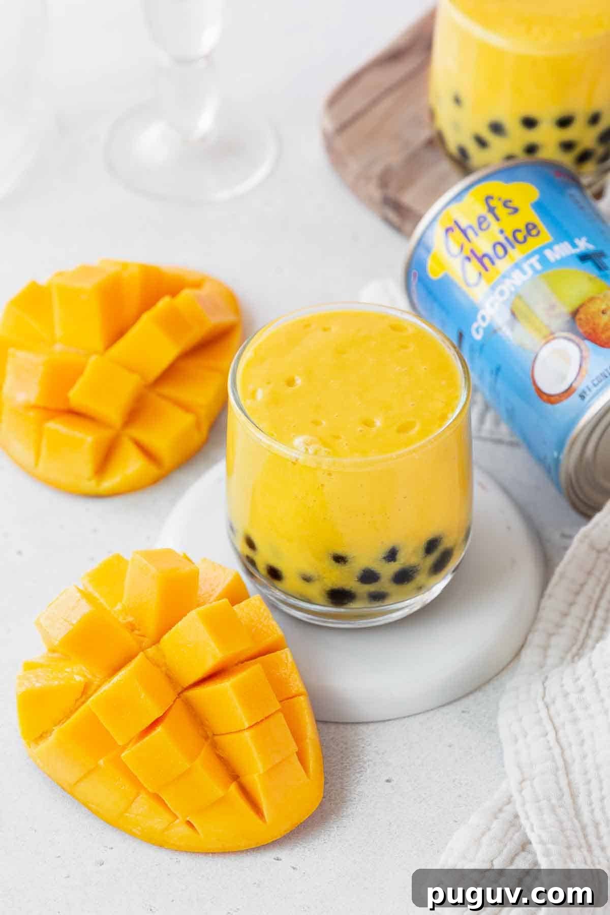 A small glass of the mango boba tea next to a can of coconut milk and a cubed mango.
