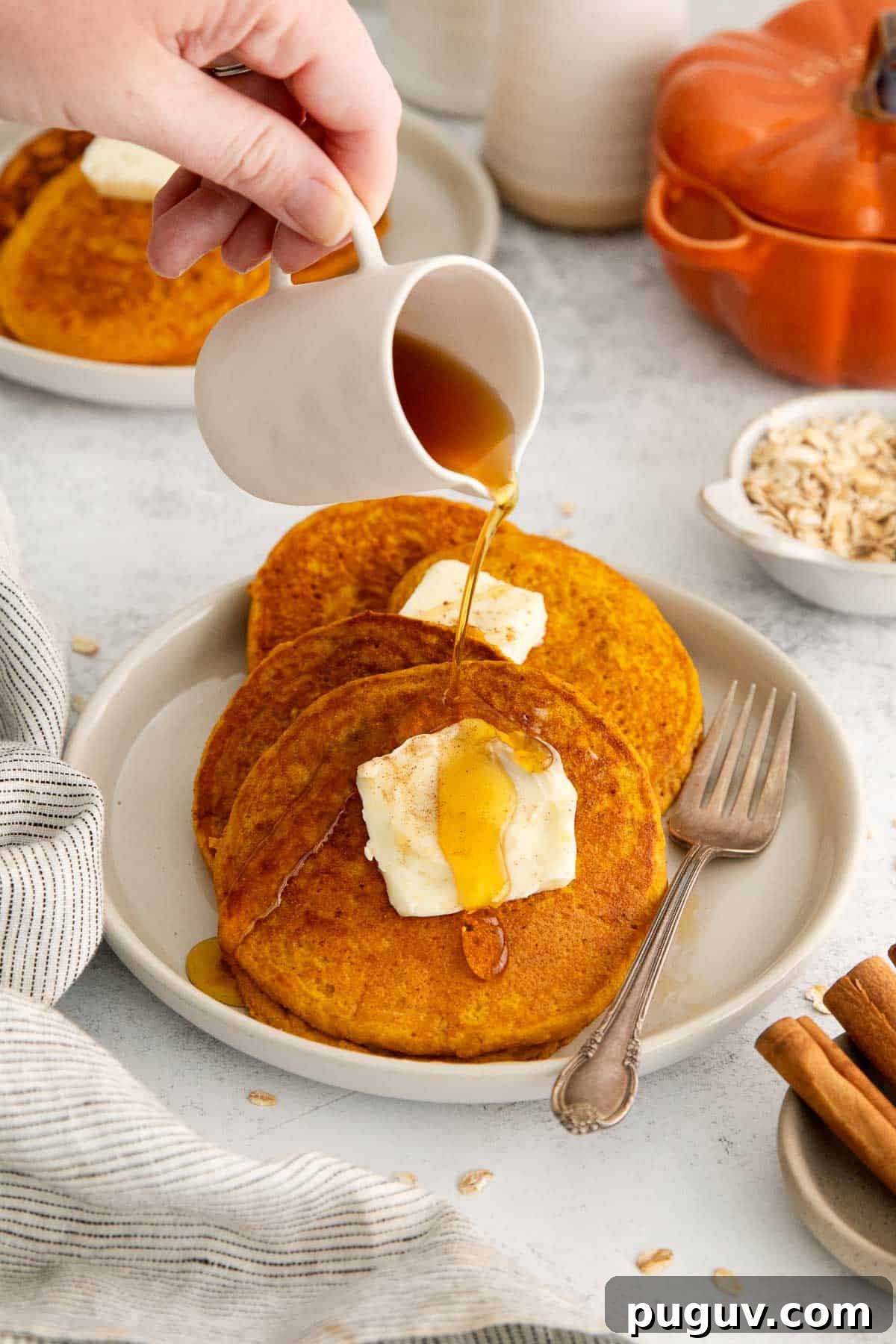 three oat flour pumpkin pancakes with butter and syrup being poured on.