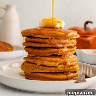 stack of oat flour pumpkin pancakes with butter and syrup being poured on top.