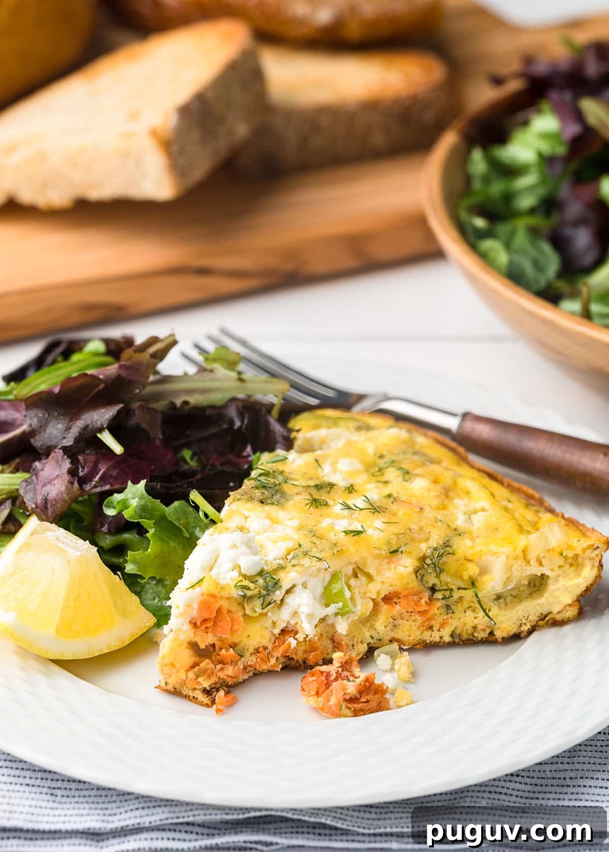 Smoked Salmon, Leek & Goat Cheese Frittata Recipe 2 slice of smoked salmon frittata on a white plate with spring greens and a lemon wedge
