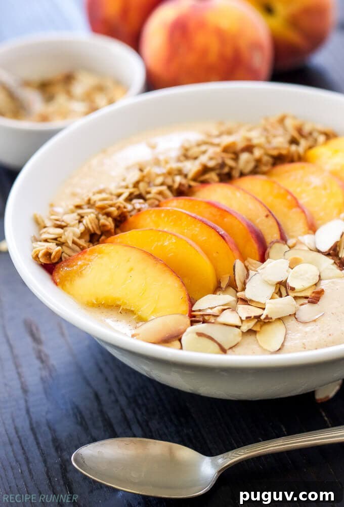 Creamy Peach Smoothie Bowl Recipe for Summer Breakfast 4 A peach smoothie in a bowl on a dark table with a spoon sitting next to it.