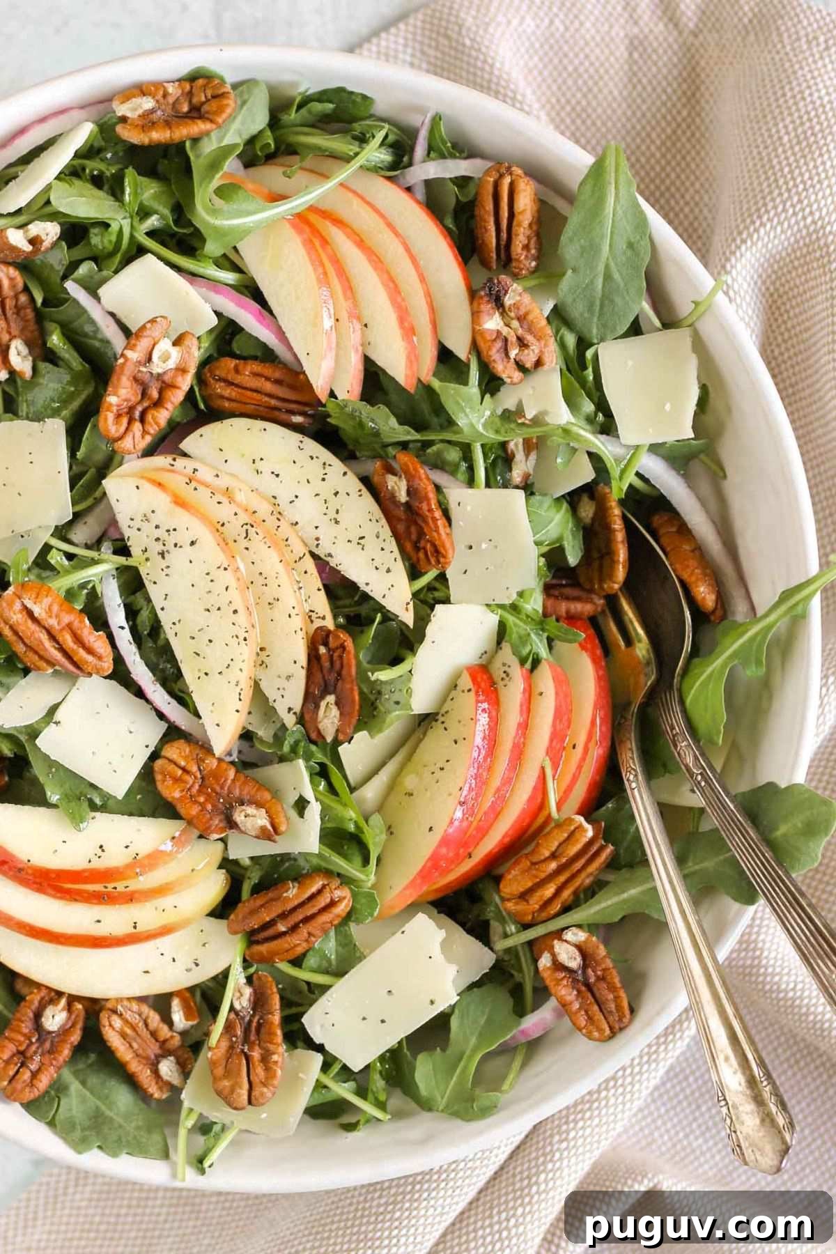Crisp Apple and Arugula Salad with Toasted Pecans 2 Arugula apple salad with pecans, parmesan cheese, and red onion in a large salad bowl with vintage utensils.