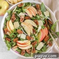 Crisp Apple and Arugula Salad with Toasted Pecans 15 Arugula and apple salad with pecans, parmesan cheese, and red onion in a large salad bowl with vintage silverware.