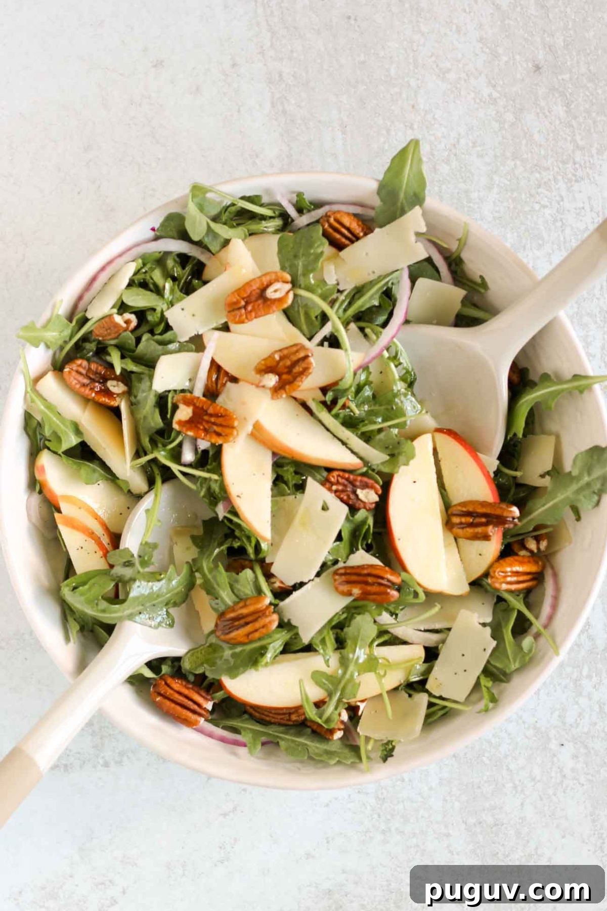 Crisp Apple and Arugula Salad with Toasted Pecans 8 Arugula and apple salad being mixed together in a large salad bowl.
