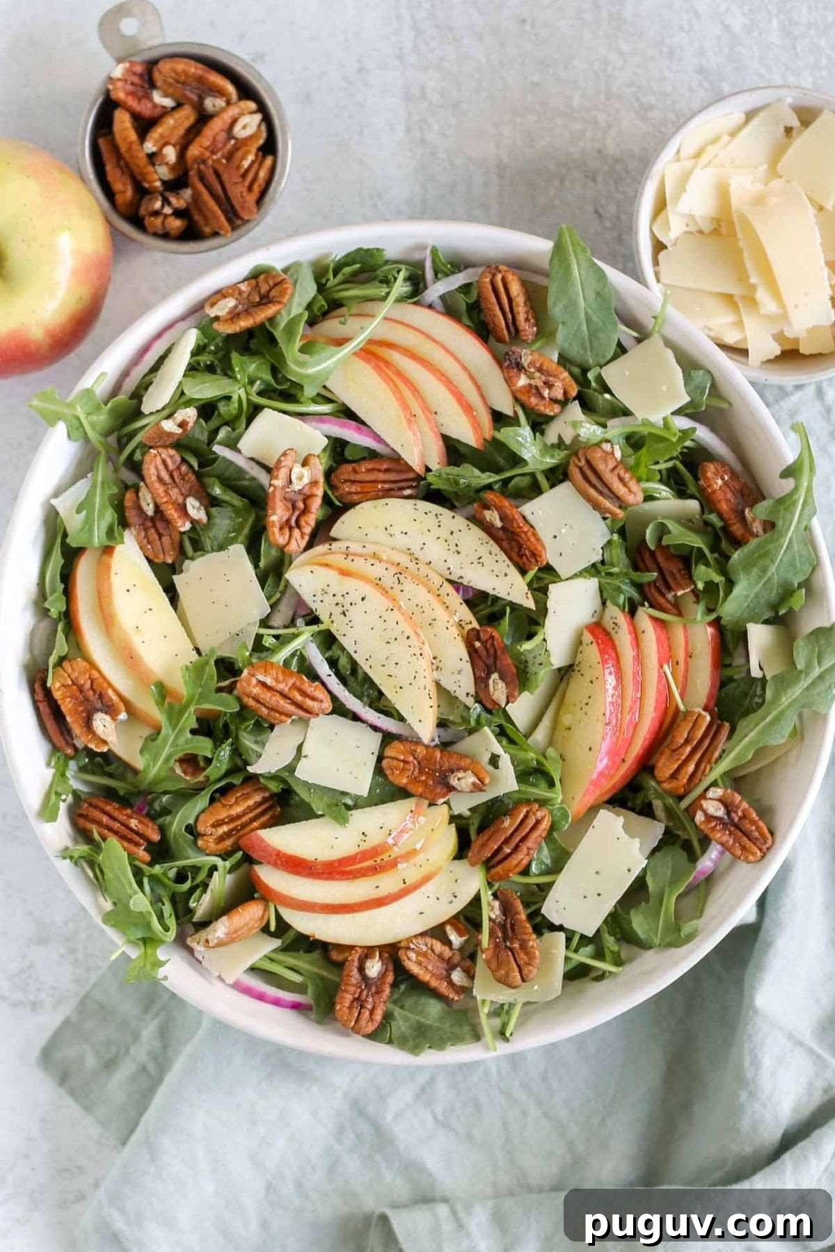 Crisp Apple and Arugula Salad with Toasted Pecans 10 Apple arugula salad in a large serving bowl with sides of parmesan cheese, pecans, and an apple.
