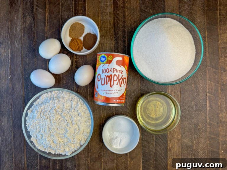 Moist Pumpkin Spice Quick Bread Recipe for Fall Baking 4 Ingredients to make pumpkin bread are eggs, canned pumpkin, flour, sugar, vegetable oil, salt, baking soda, cloves, cinnamon, allspice and nutmeg on a wooden counter.