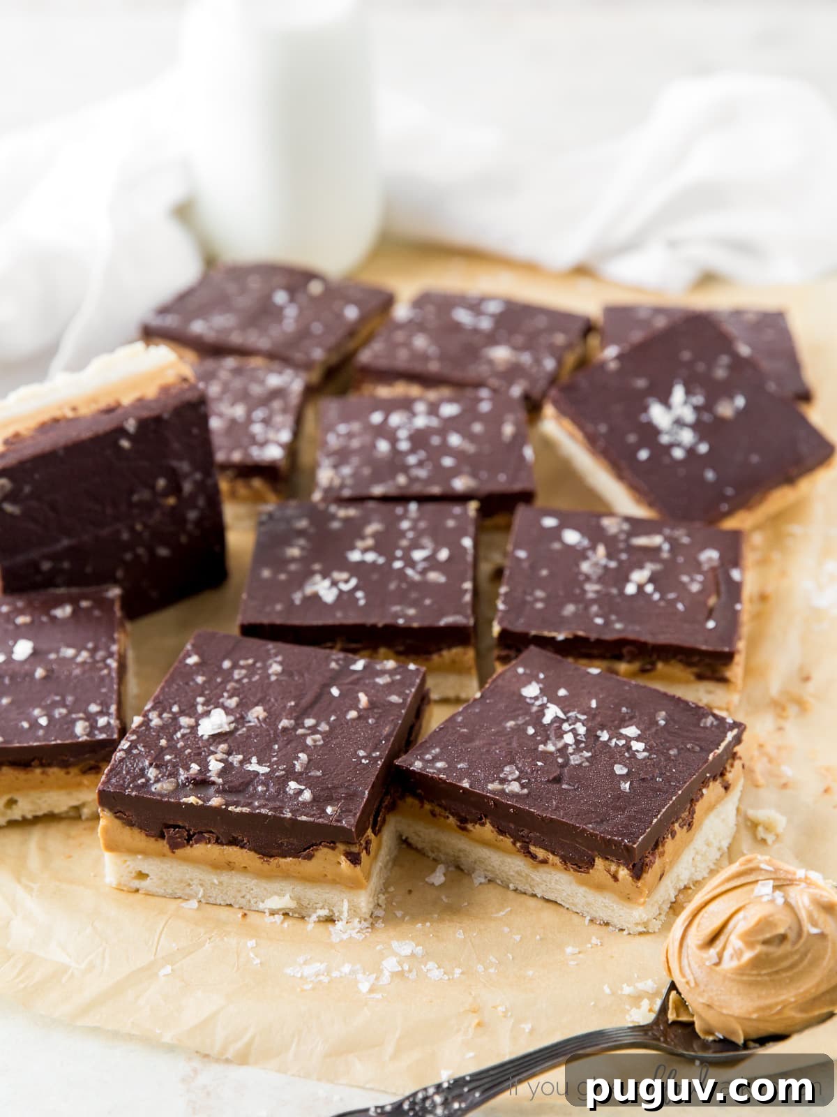 Chocolate Peanut Butter Bars with Shortbread Crust 6 peanut butter chocolate bars with sea salt on parchment paper with spoon of peanut butter
