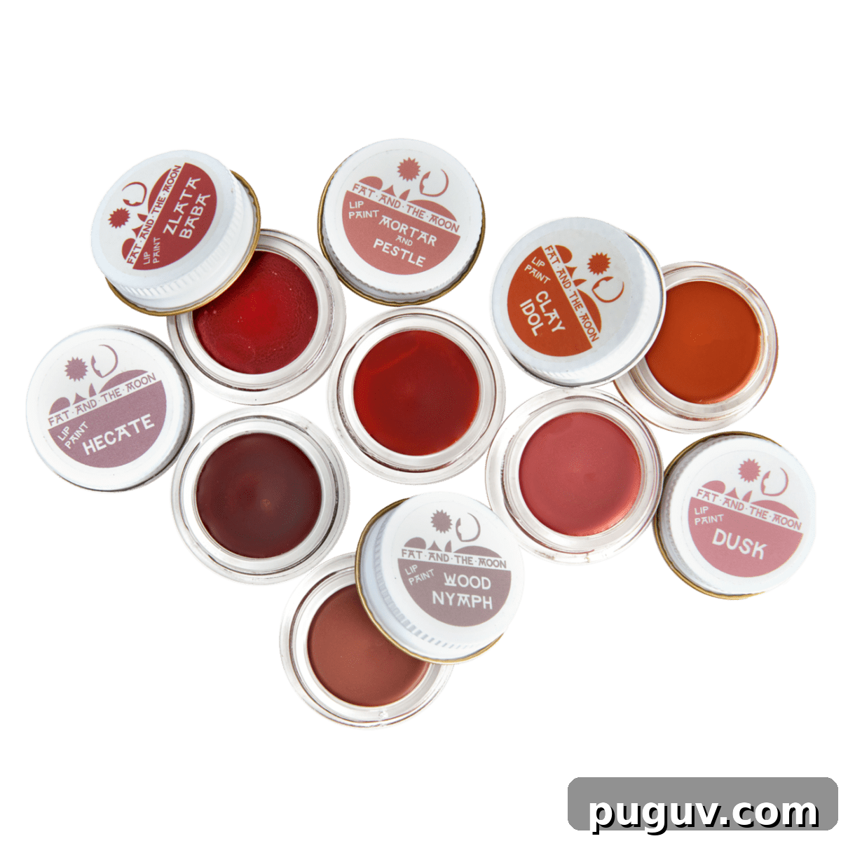 Clean Makeup for Tweens: 8 Safe Brands for Kids and Teens 12 An overhead flat-lay displays nine small open pots of natural tinted lip balm or cheek stain from Fat and The Moon in shades of reddish-pink and brown, with their labeled white lids scattered around them on a black background.