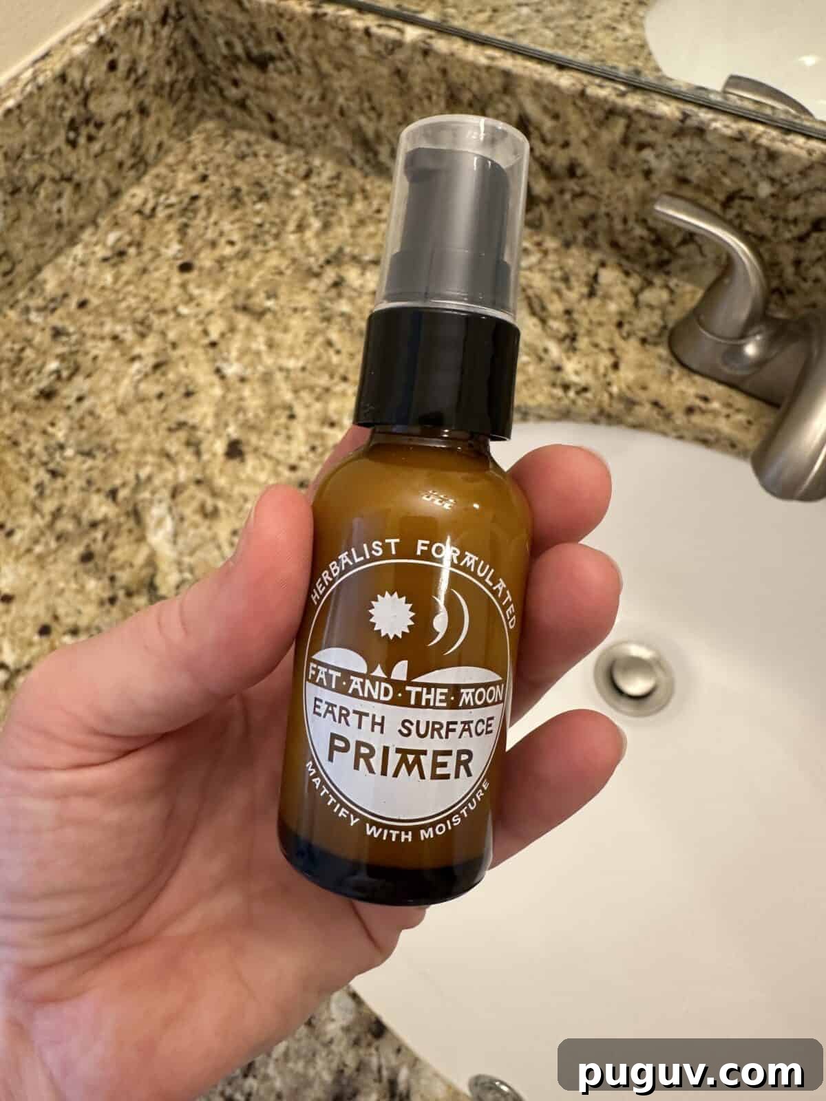 Clean Makeup for Tweens: 8 Safe Brands for Kids and Teens 13 A person is holding a small, brown glass bottle of Fat and the Moon Earth Surface Primer over a white bathroom sink with a marble countertop.