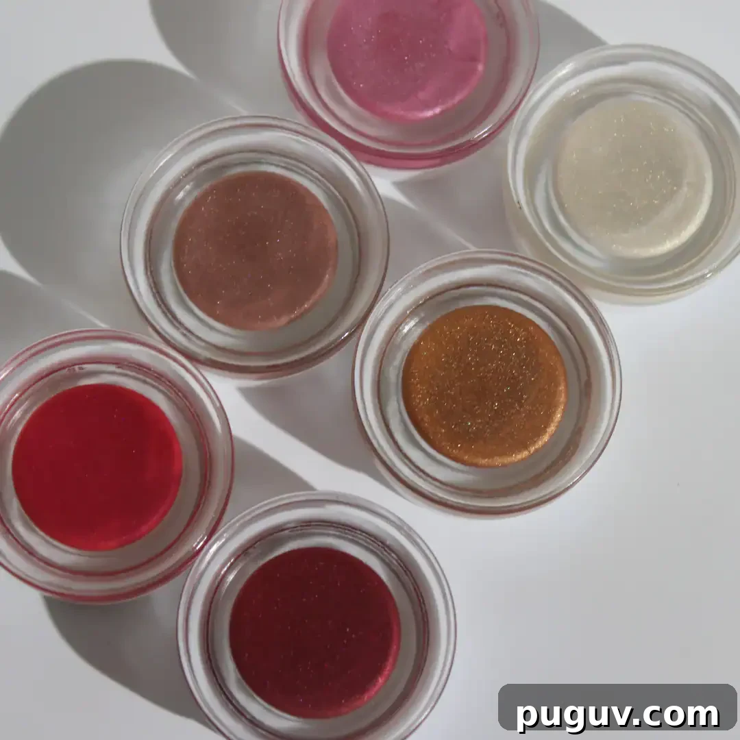 Clean Makeup for Tweens: 8 Safe Brands for Kids and Teens 7 An overhead shot displays six small glass pots containing shimmering natural play makeup from Honey in shades of pink, red, bronze, gold, and clear gloss on a white surface.