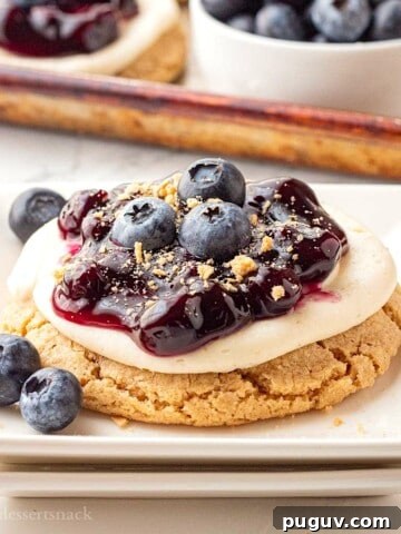 Blueberry pie filling on top of cheesecake cookie on white plate.