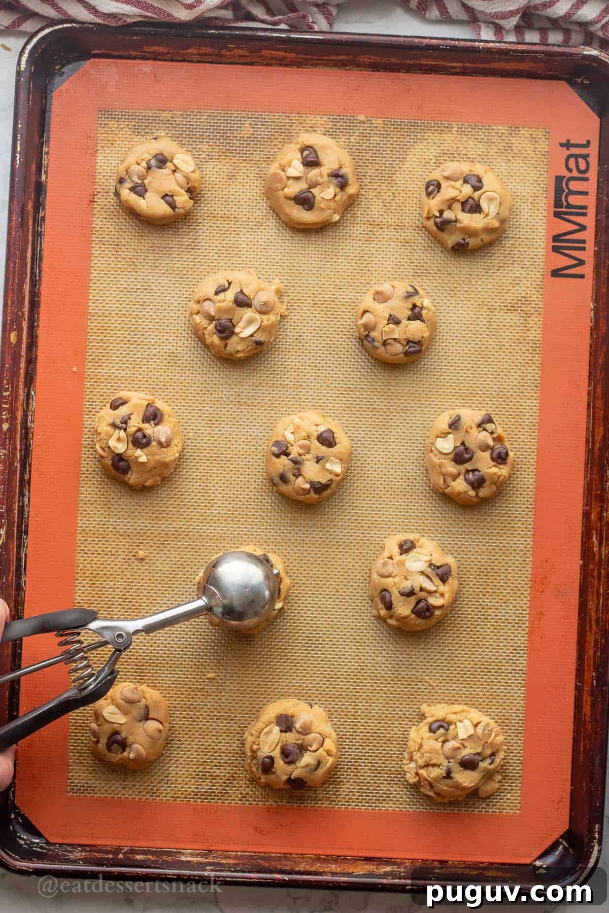 Raw cookie dough balls on baking sheet with cookie scoop.
