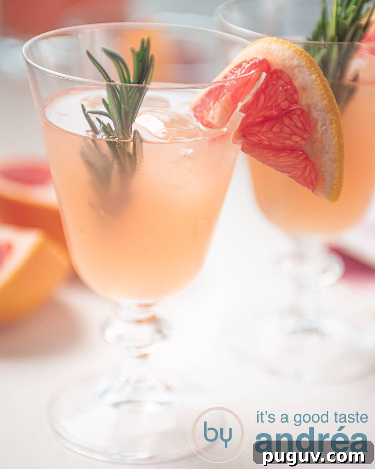A glass filled with a rosemary grapefruit mocktail. Garnished with rosemary and slices grapefruit