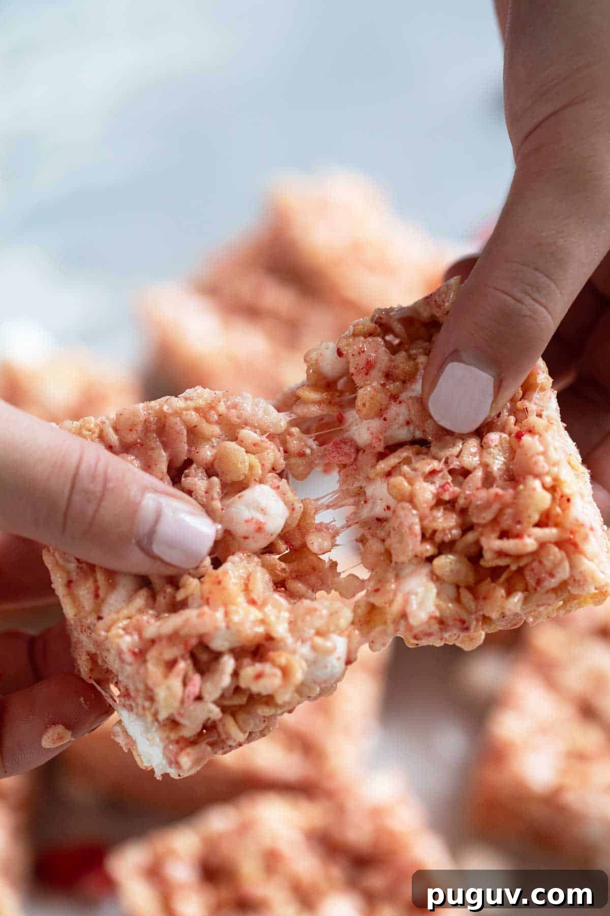 Strawberry Rice Krispie Treats Recipe — Quick No-Bake Dessert 10 Fingers pulling a strawberry Rice Krispie treat apart.