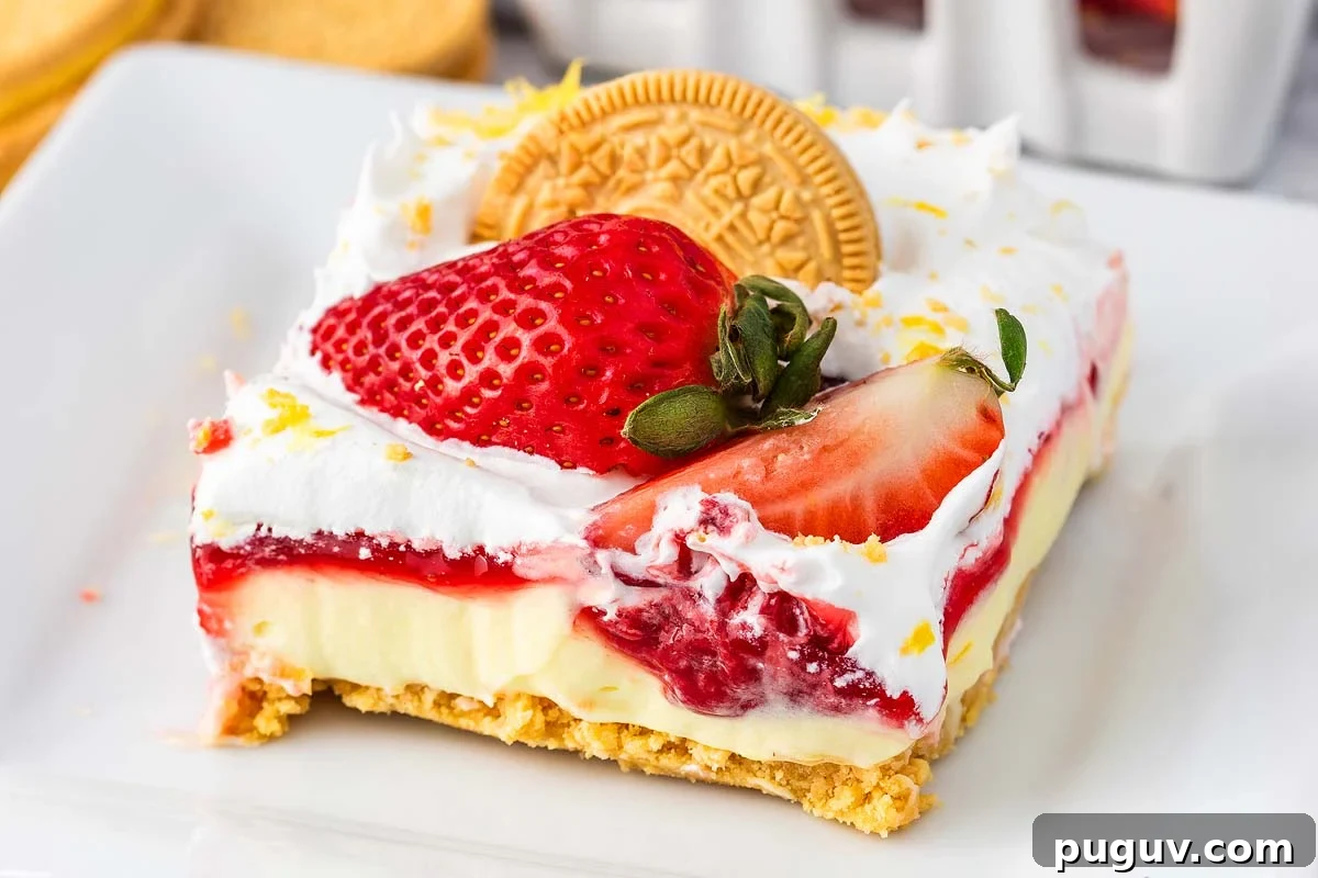 A square slice of strawberry lemon cheesecake lasagna featuring a cracker crust, a luscious cream filling, a tangy strawberry topping, whipped cream, and topped with a whole golden cookie and fresh strawberries.