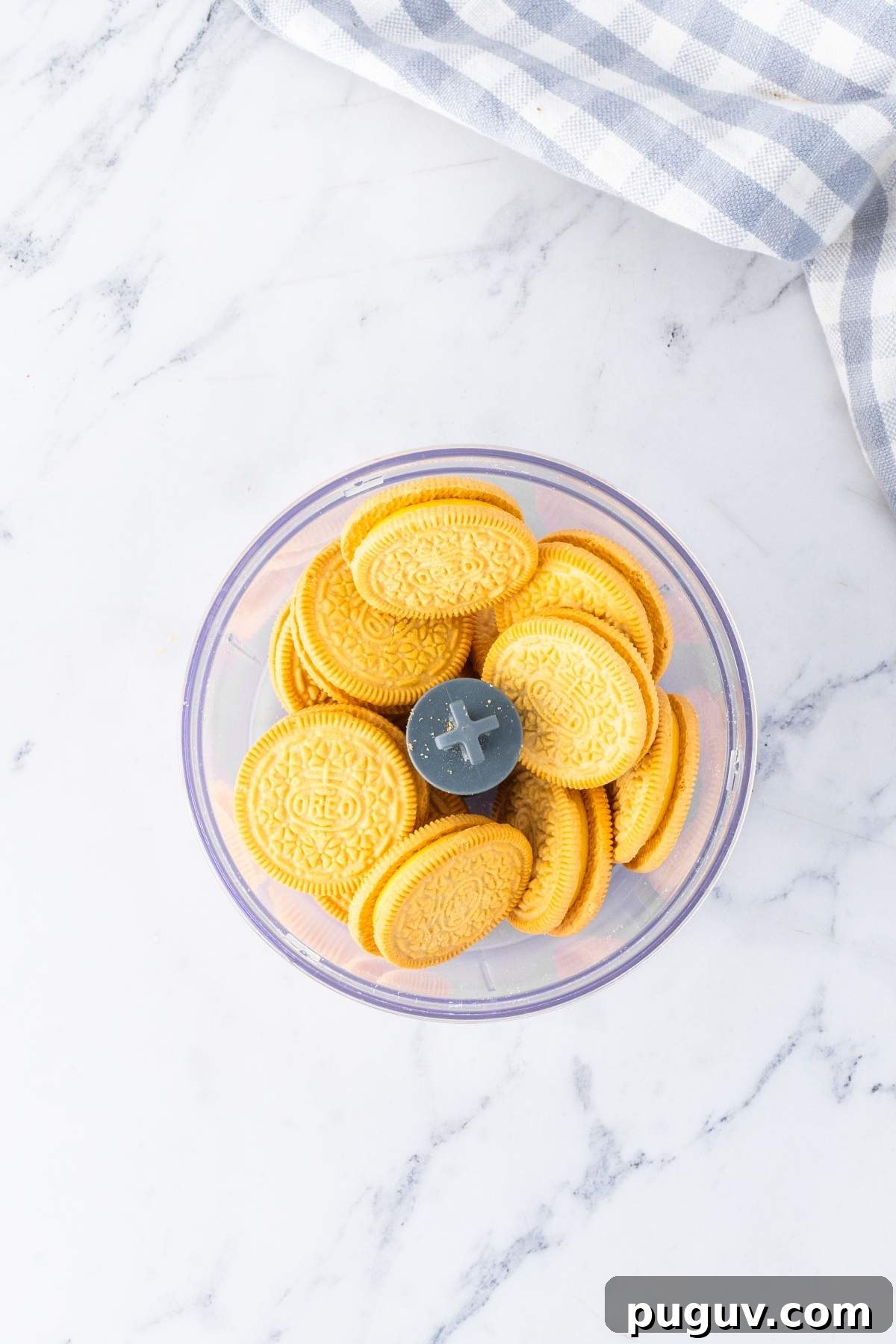 A bowl of yellow sandwich cookies placed on a marble surface next to a blue and white checkered cloth, reminiscent of the vibrant flavors in a strawberry lemon cheesecake.