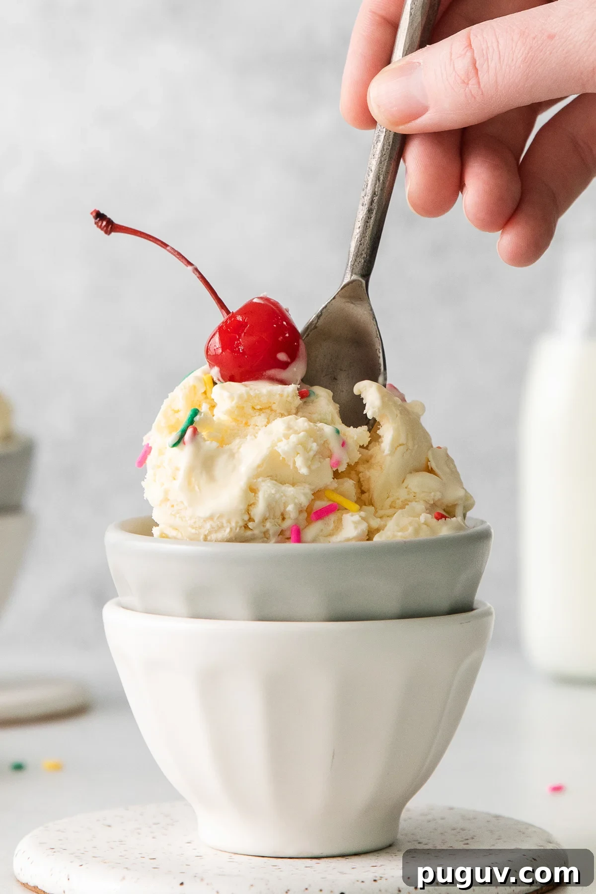 a person scooping ice cream into a bowl with a cherry on top.