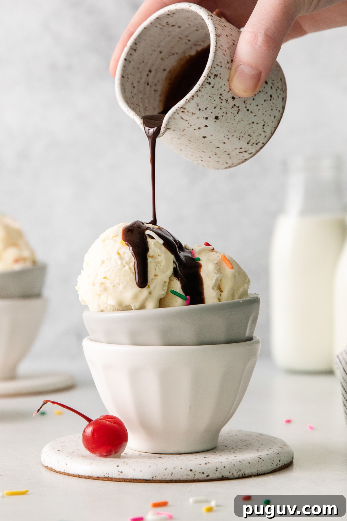 a person pouring ice cream into a bowl with a cherry on top.