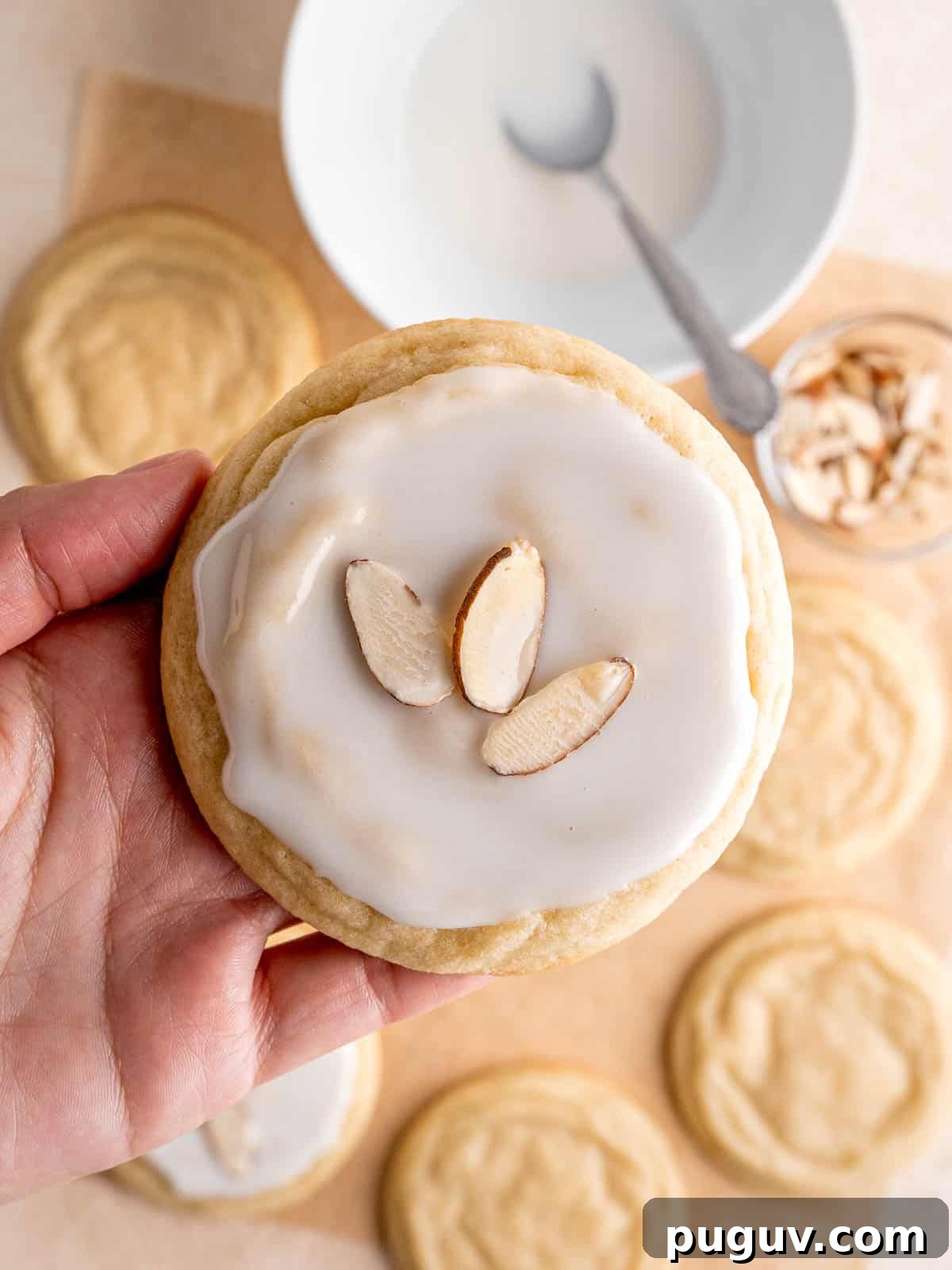 Soft Almond Sugar Cookies with Melt-In-Your-Mouth Texture 8 A hand holding an almond cookie with icing and sliced almonds on top.