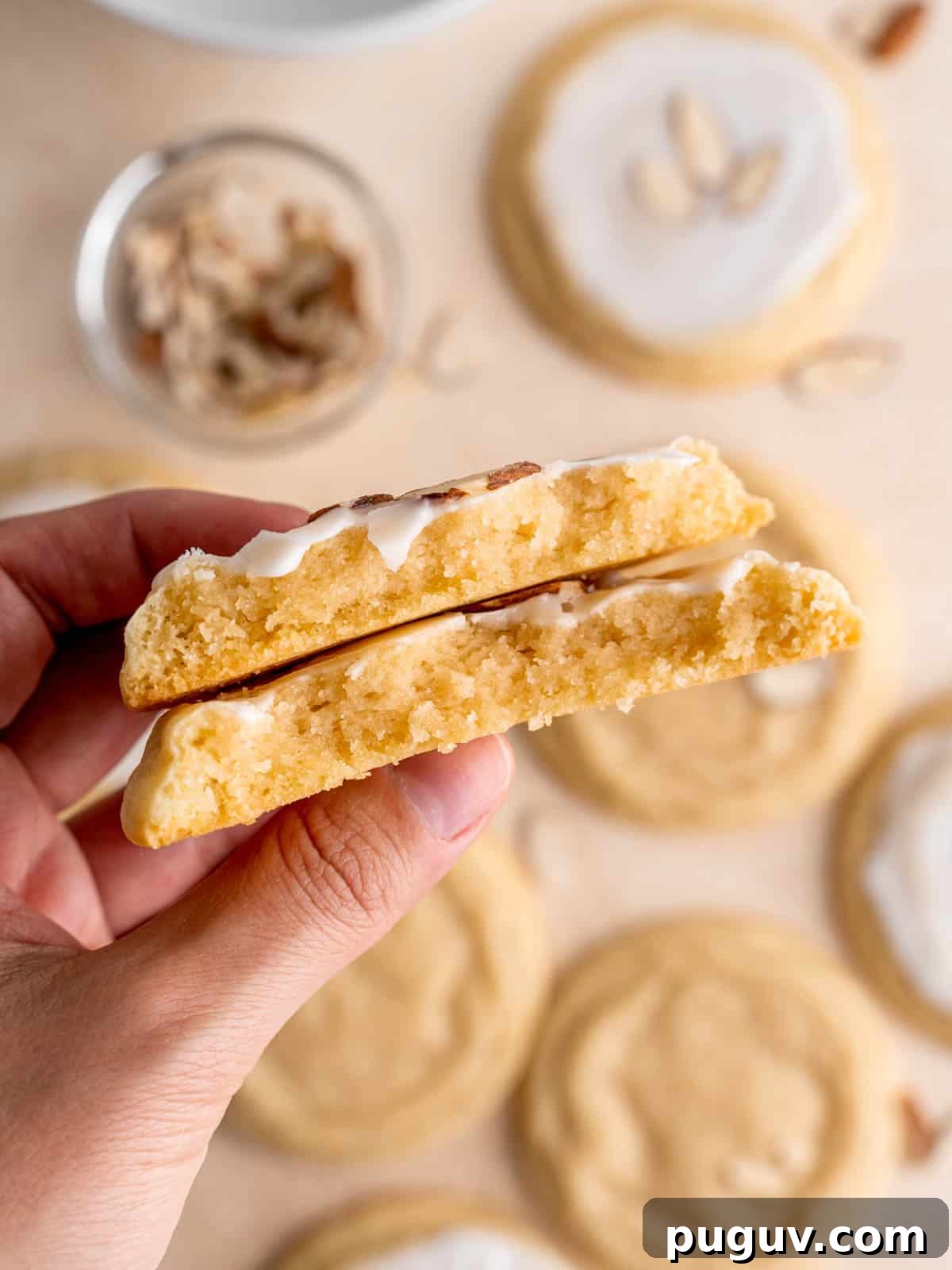Soft Almond Sugar Cookies with Melt-In-Your-Mouth Texture 9 A hand holding two halves of a soft iced almond cookie.