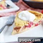 Red Fruit Custard Cake: Elegant Summer Dessert with Fresh Berries 5 Horizontal image of a slice of dessert filled with strawberry and raspberry topped with whipped cream on a white square plate next to a fork and pink napkin.