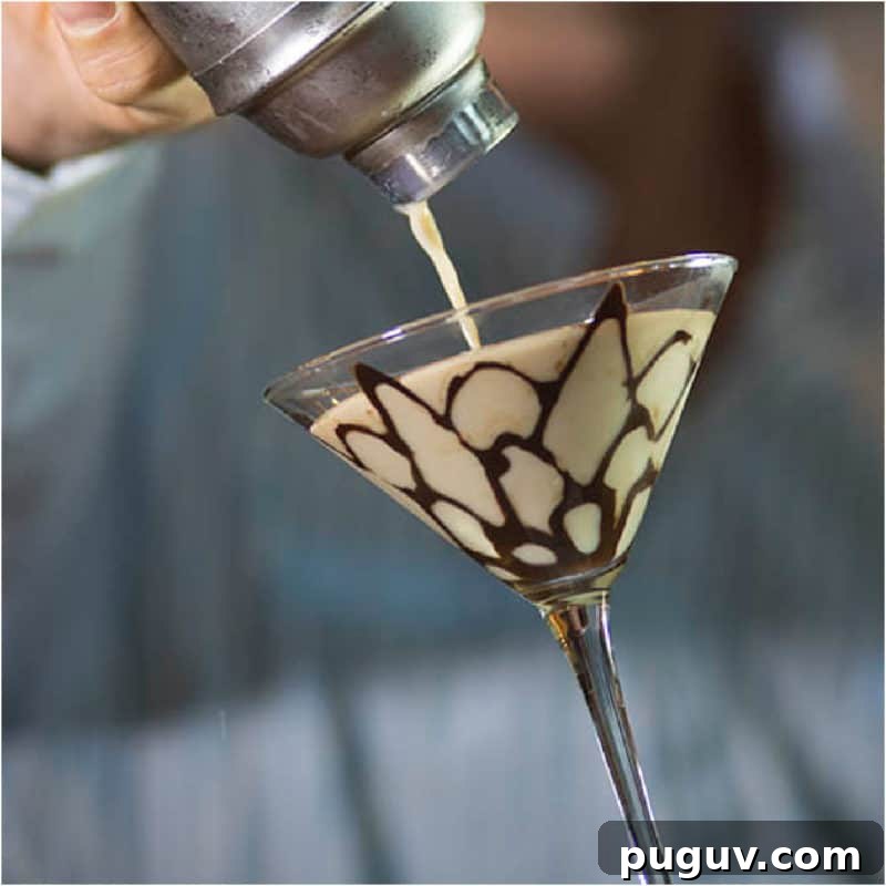 Christmas Cocktail Recipes Everyone Will Love 14 Tiramisu Martini pouring from a cocktail shaker into a martini glass with chocolate design.