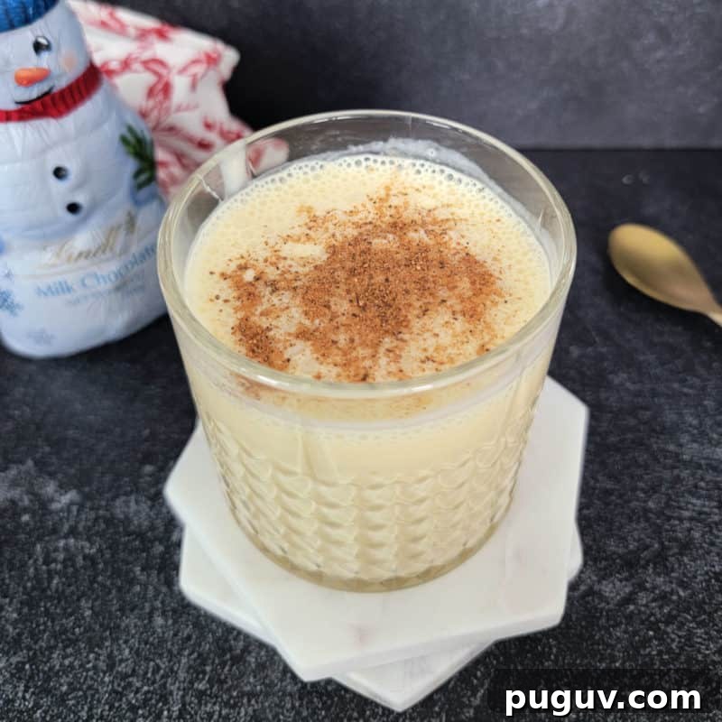 Christmas Cocktail Recipes Everyone Will Love 20 Bourbon Eggnog in a crystal glass on white coasters next to a gold spoon and snowman