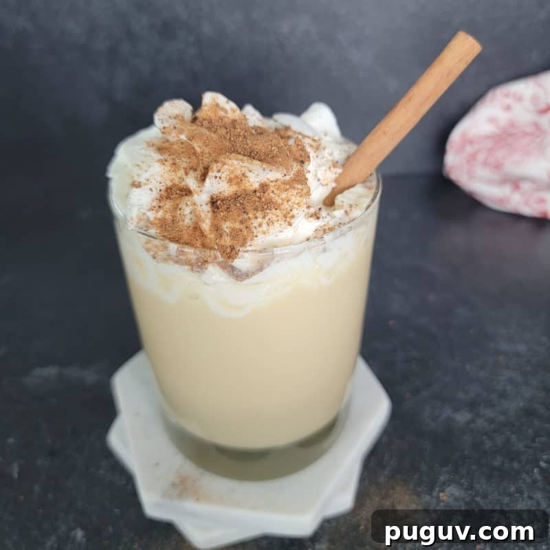 Christmas Cocktail Recipes Everyone Will Love 24 Eggnog Mudslide in a glass on a white coaster garnished with whipped cream and nutmeg with a cinnamon stick