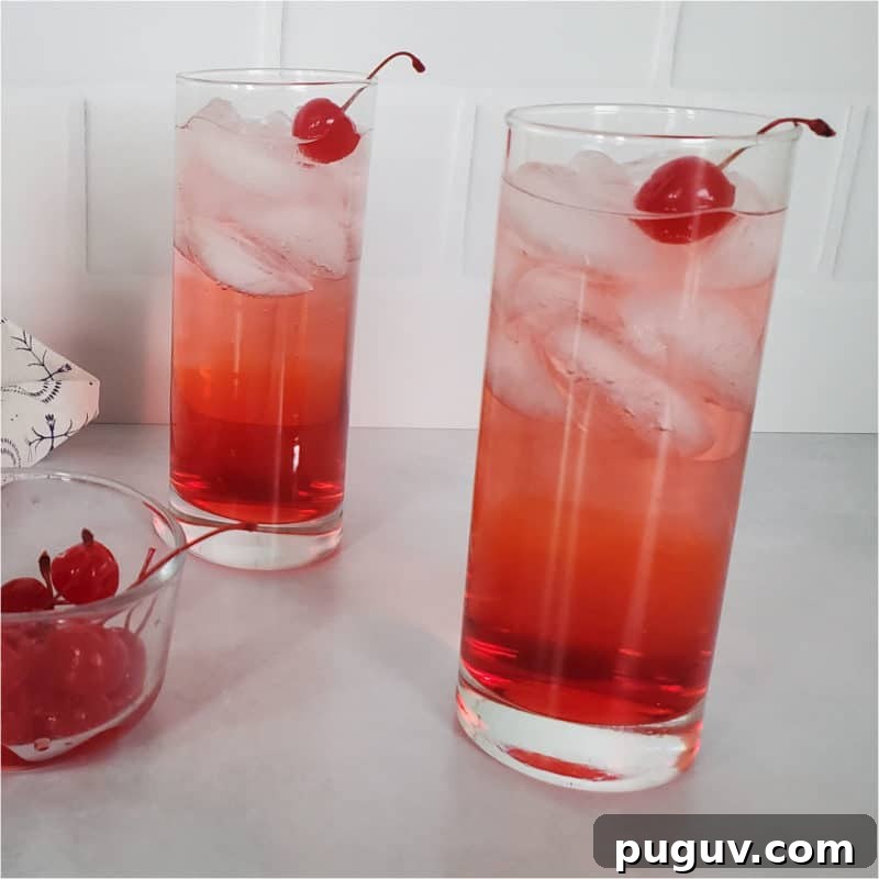 Christmas Cocktail Recipes Everyone Will Love 7 Two red cocktails in tall glasses garnished with maraschino cherries next to a bowl of cherries