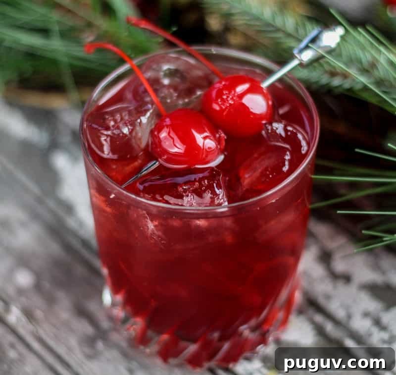 Christmas Cocktail Recipes Everyone Will Love 10 red cherry cocktail with two maraschino cherries for garnish next to greenery