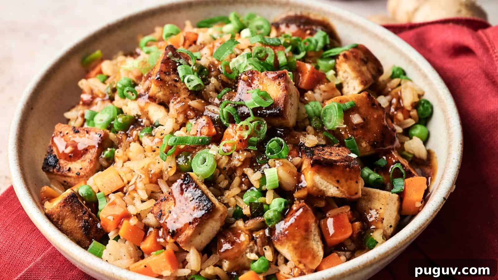 15 Chinese Dishes That Let You Cook Dinner in 30 Minutes 11 A bowl of fried rice with grilled tofu, diced carrots, peas, chopped green onions, and a drizzle of dark sauce, served on a red cloth.