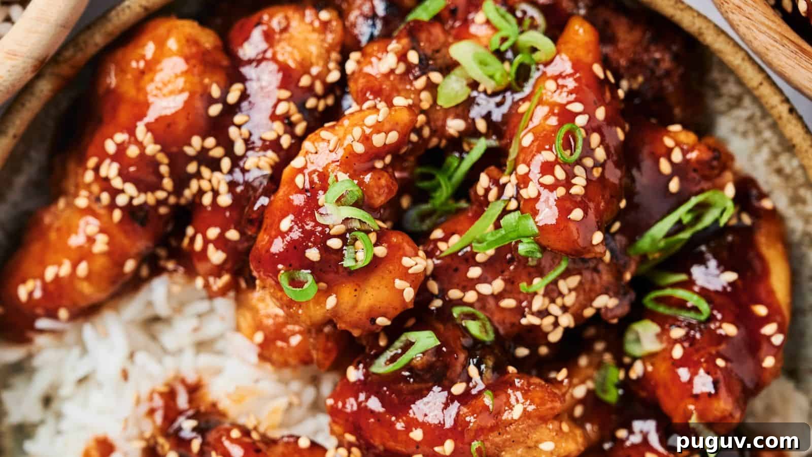 15 Chinese Dishes That Let You Cook Dinner in 30 Minutes 12 A close-up of glazed chicken pieces with sesame seeds and chopped scallions on a bed of rice.