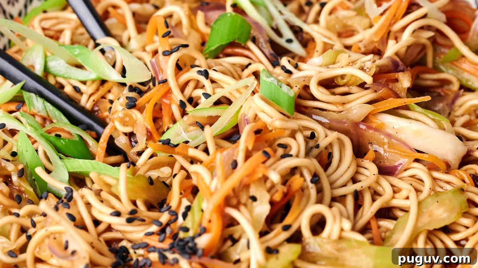 15 Chinese Dishes That Let You Cook Dinner in 30 Minutes 16 A close-up view of a plate of chow mein stir-fried noodles with vegetables and black sesame seeds, with chopsticks visibly picking up a portion.