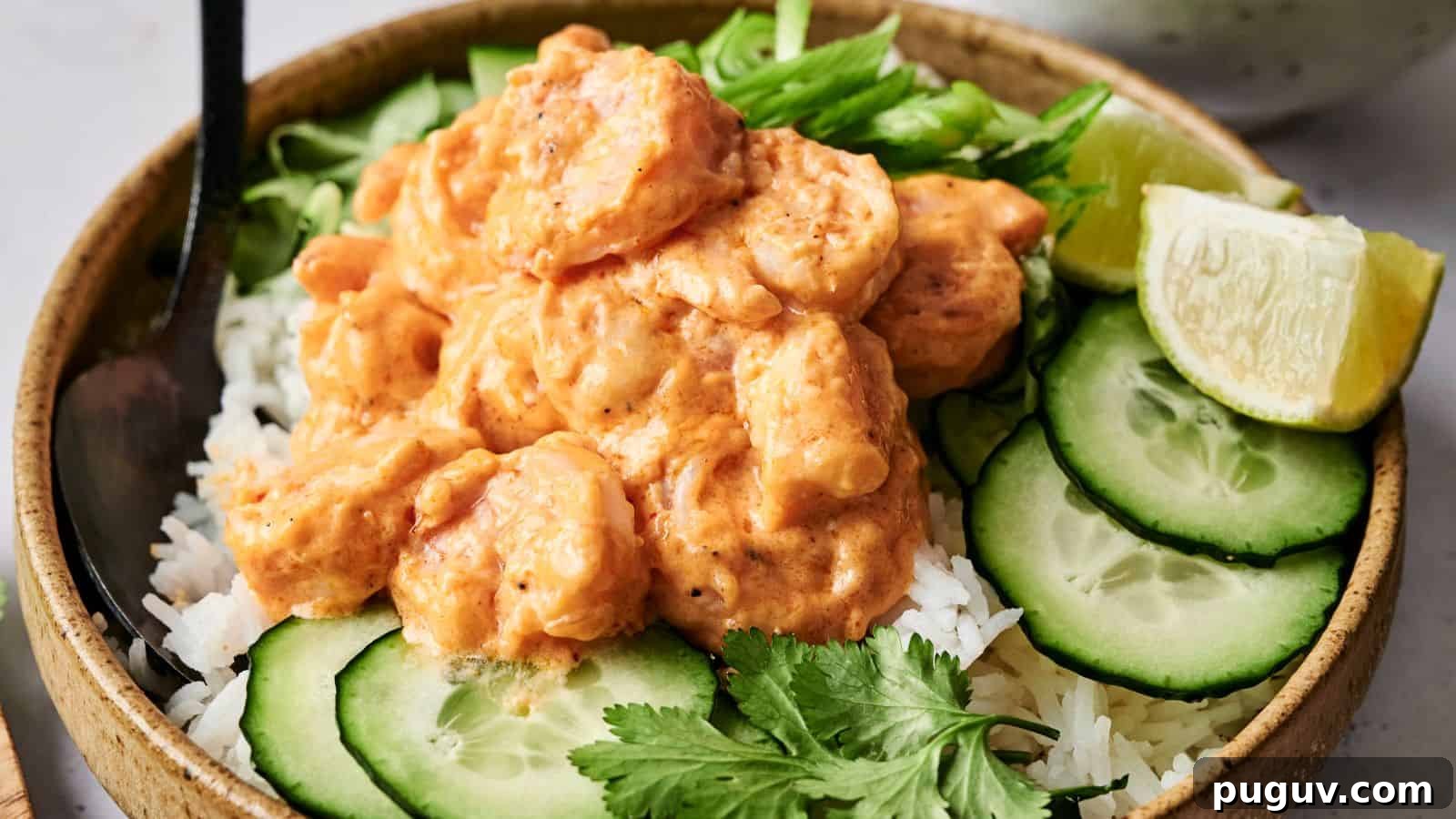 15 Chinese Dishes That Let You Cook Dinner in 30 Minutes 6 A bowl of rice topped with shrimp in a creamy sauce, garnished with cucumber slices, lime wedge, cilantro, and sliced green onions.