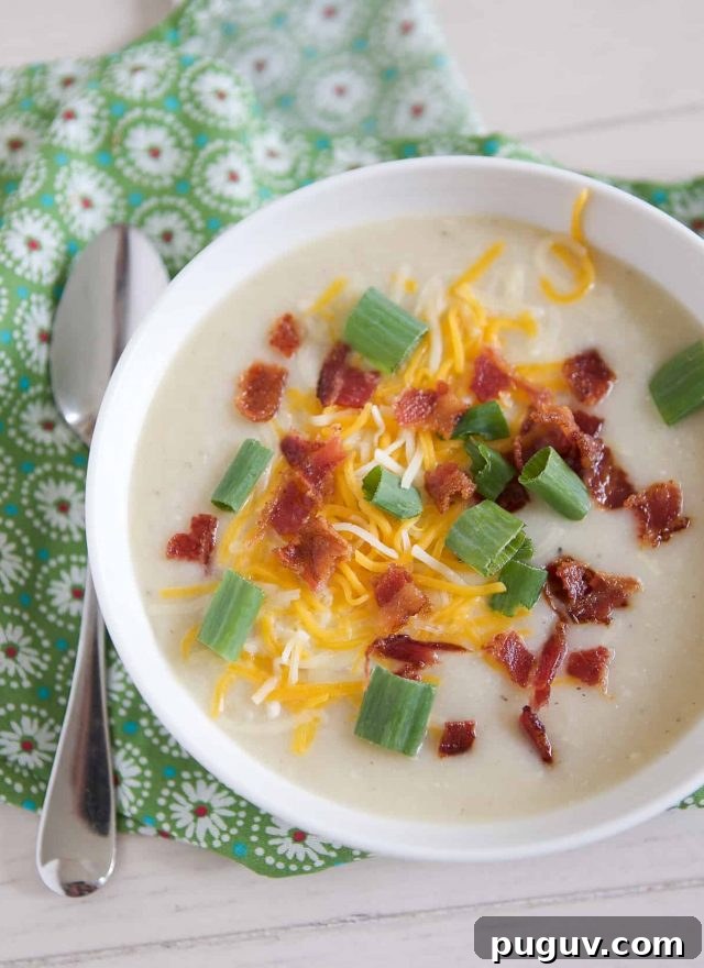 overhead shot of white bowl filled with cauliflower potato soup topped with cheese, green onion and bacon