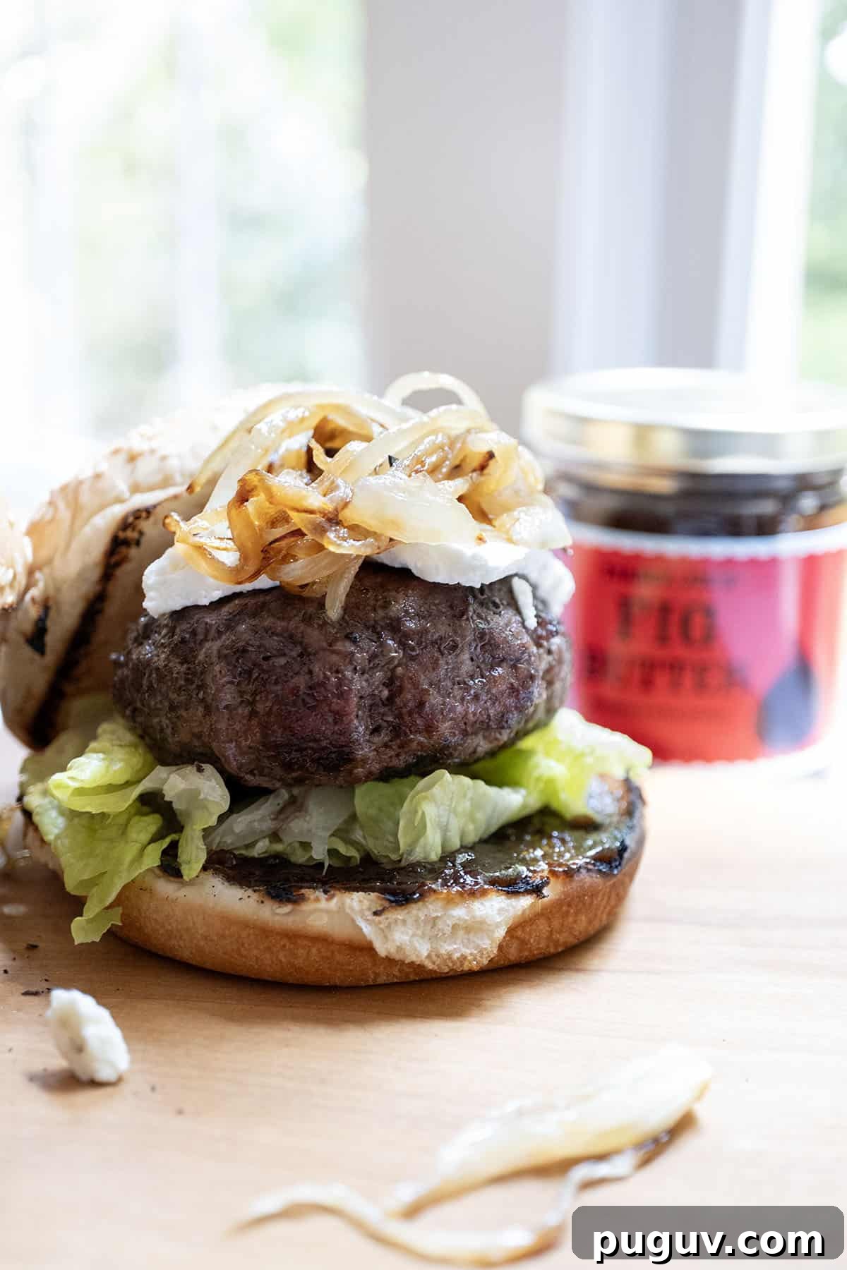 Fig Jam & Goat Cheese Burger Recipe for Sweet Savory Flavor 2 burger on a bed of lettuce with fig jam underneath, topped with goat cheese and caramelized onions.