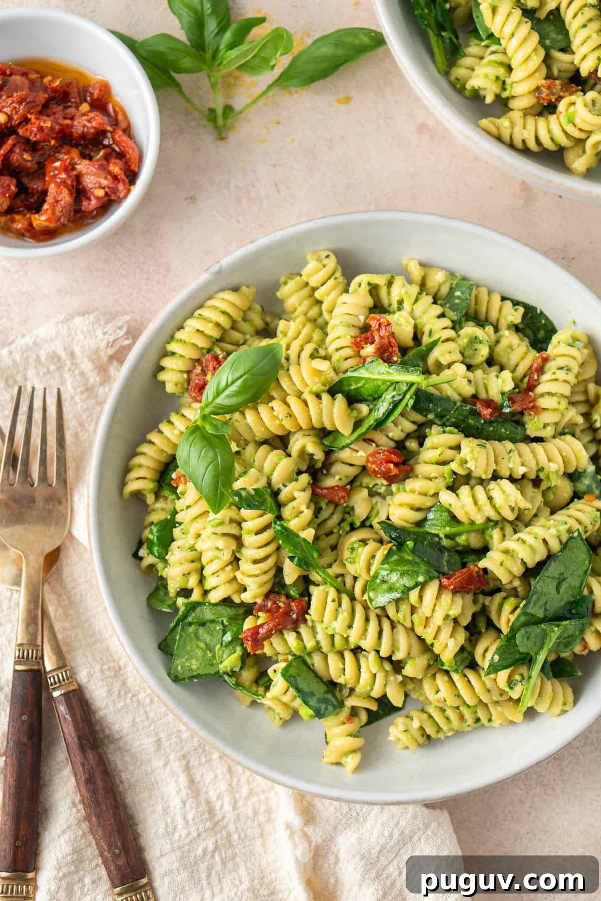 Close up of a bowl of pea pesto pasta with spinach and sundried tomatoes with forks on the side.