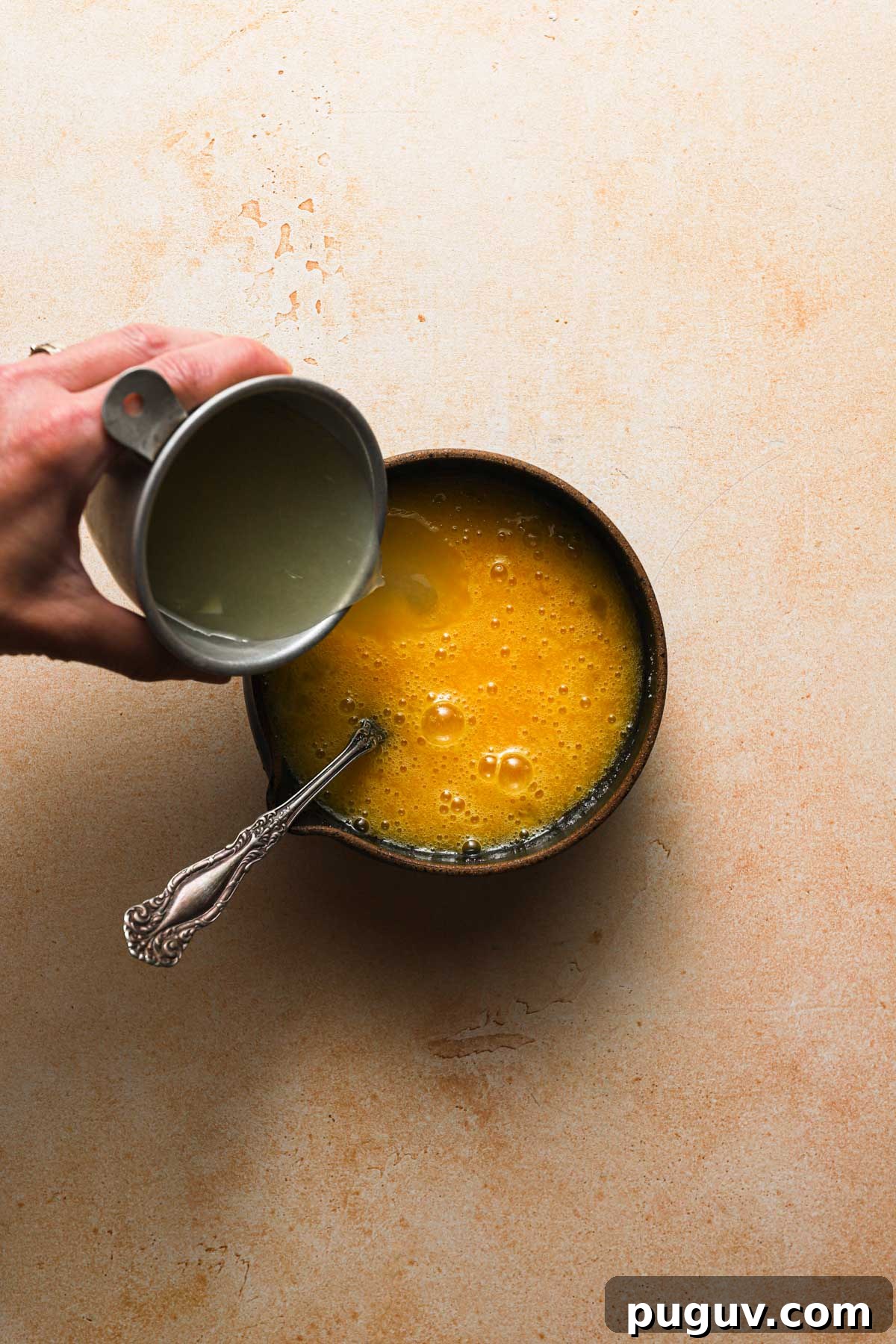 Pouring lemon juice into a bowl with egg mixture.