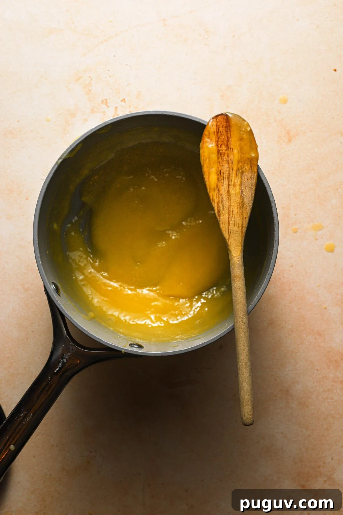 Thickened lemon curd in a saucepan with a wooden spoon on top.