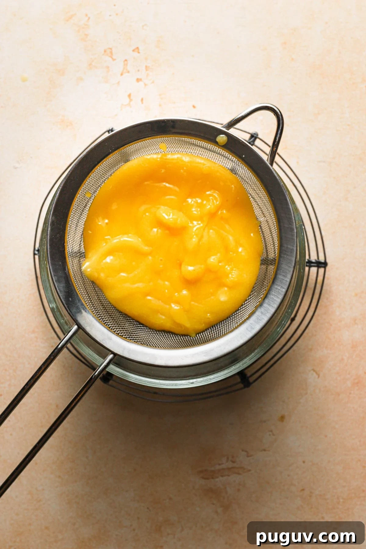 Lemon curd over in a sieve over a bowl.