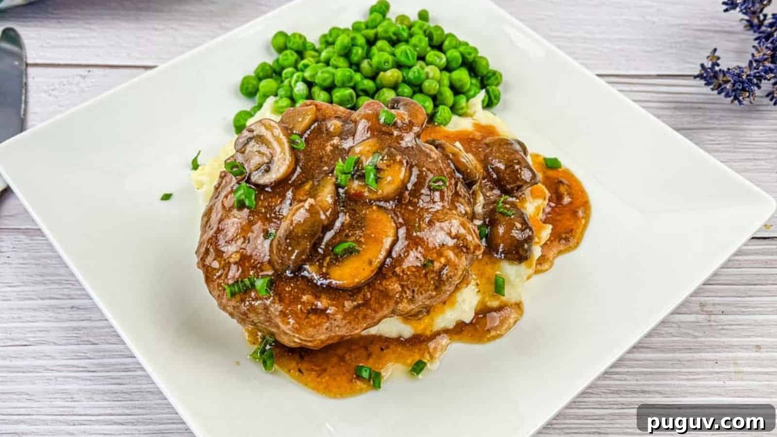 17 Low-Carb Meals That Keep You Full, Energized, and Ready 15 A white plate with Salisbury steak topped with mushroom gravy on mashed potatoes, accompanied by a side of green peas.