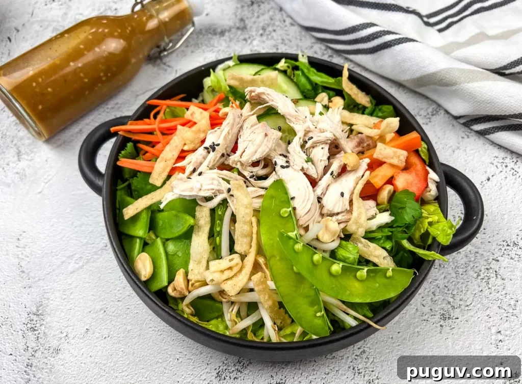 17 Low-Carb Meals That Keep You Full, Energized, and Ready 10 A bowl of Chinese chicken salad with shredded chicken, snap peas, carrots, and peppers, accompanied by a bottle of dressing on the side.