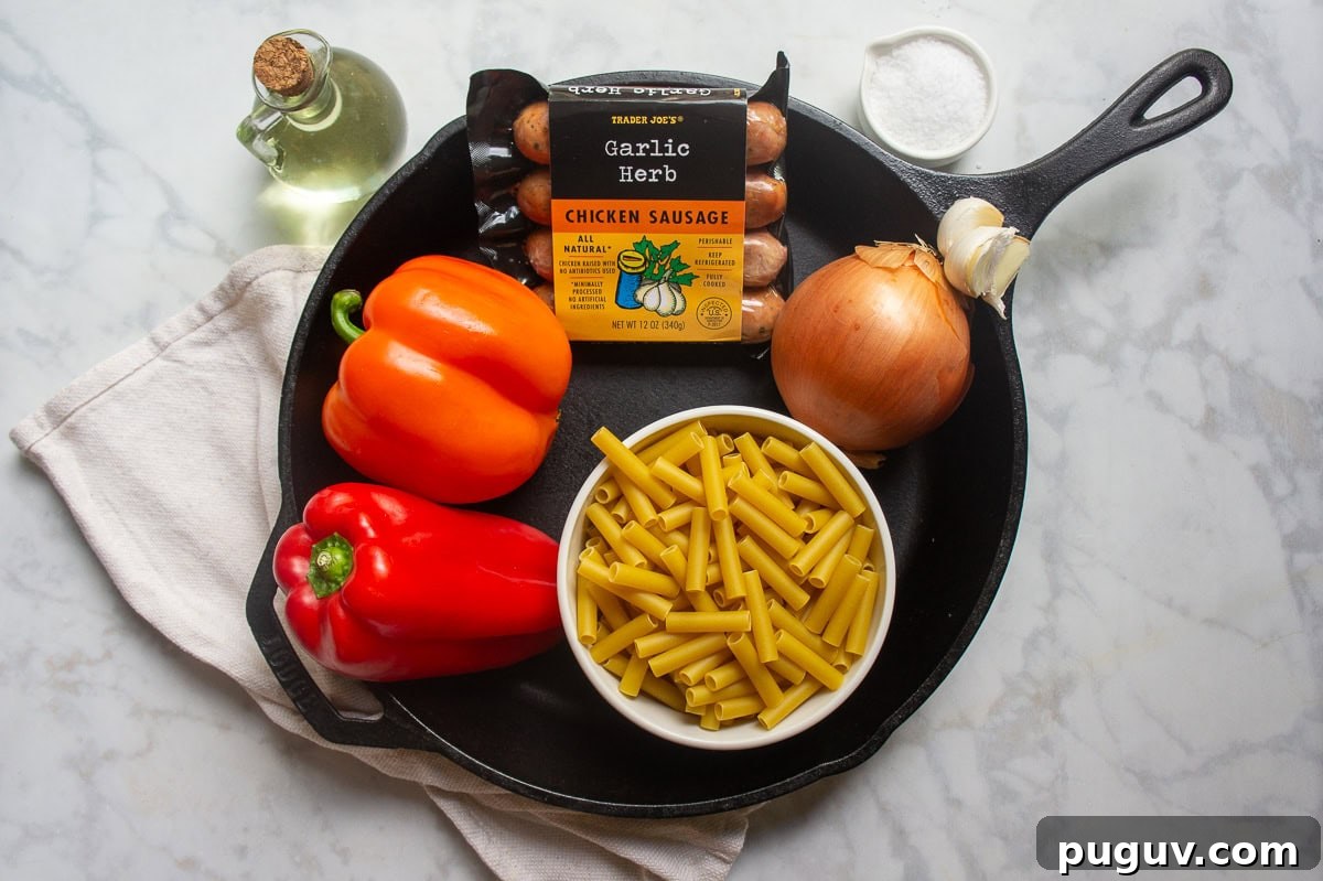 Sausage and Pepper Pasta Recipe — Quick Weeknight Dinner 3 A cast iron pan with two fresh bell peppers, dried ziit pasta, an onion, and a package of sausage inside it.